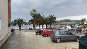A parking area with several cars, palm trees, and a view of the sea. - Apartments Pinsa (Okrug)
