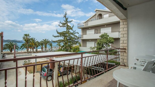 A balcony with a view of the sea, a parked car, and a table with chairs. - Apartments Pinsa (Okrug)