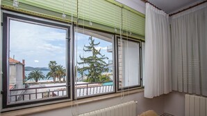 A room with a large window overlooking a pool and palm trees, a radiator, and a brown chair. - Apartments Pinsa (Okrug)