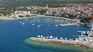 A coastal town with a marina filled with boats, a prominent church spire, and a backdrop of hills. - Apartments Gorana Novi V (Novi Vinodolski)