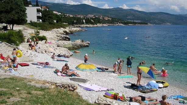 A beach with people sunbathing, swimming, and using beach umbrellas. - Apartments Gorana Novi V (Novi Vinodolski)