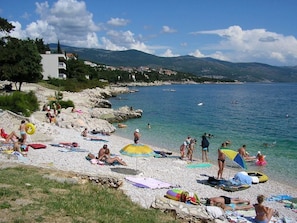 Una playa con gente tomando el sol, nadando y usando sombrillas.