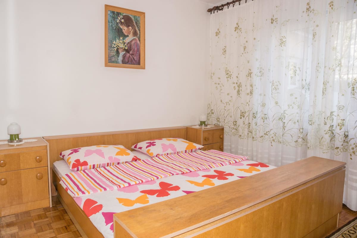 A bedroom with a wooden bed, floral curtains, a nightstand with a lamp, and a painting on the wall.