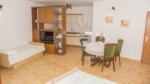 A compact room with a bed, a wooden wardrobe, a dining table with chairs, a kitchen area, and a small window. - Apartments Gorana Novi V (Novi Vinodolski)