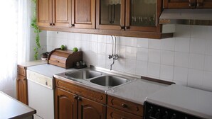 A kitchen with wooden cabinets, a double sink, and a built-in oven. - Apartments Gorana Novi V (Novi Vinodolski)