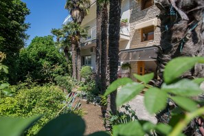 A multi-story building with balconies, surrounded by lush greenery and palm trees. - Apartments Lončar (Kastela)