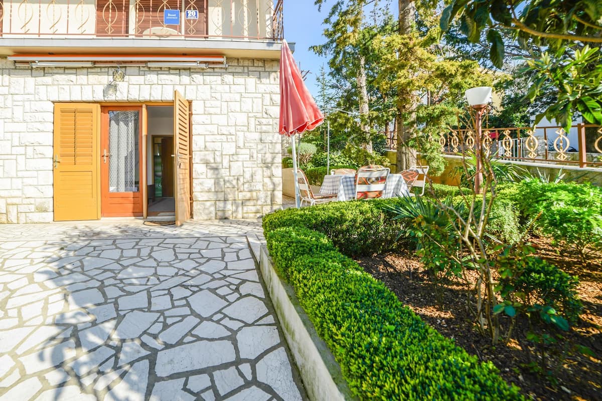 A stone building with a wooden door, a red umbrella, and a paved walkway.