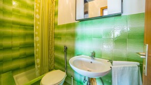 Ein Badezimmer mit grünen Fliesenwänden, einem weißen Waschbecken und einer Toilette.