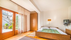 Ein Schlafzimmer mit einem hölzernen Bett, einem Fernseher und einer Glastür zum Balkon.