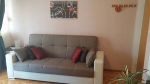 Ein graues Sofa mit roten und grauen Kissen, ein Wandbild und eine kleine Pflanze.