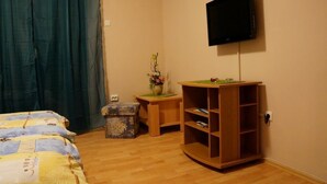 Ein Schlafzimmer mit einem Bett, einem Nachttisch aus Holz, einem an der Wand befestigten Fernseher und einem kleinen Tisch mit einer Blumenvase.