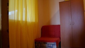 Ein kleines Zimmer mit einem Holzschrank, einem roten Bett und einem gelben Vorhang.