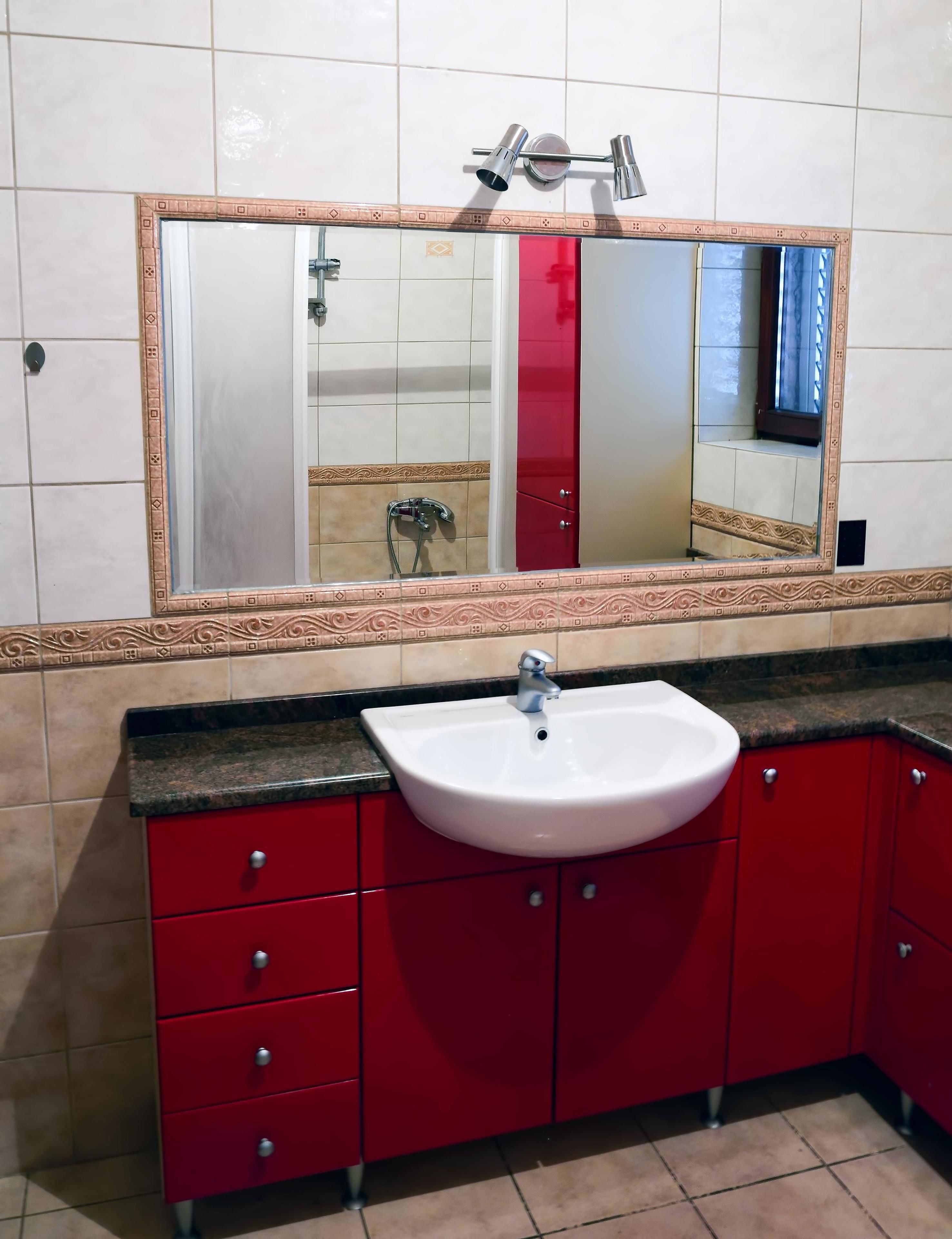 A bathroom with a white sink, red cabinets, and a large mirror with a decorative frame.