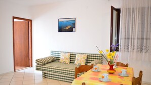 Un comedor con una mesa dispuesta para cuatro personas, un sofá con cojines estampados y un cuadro en la pared.