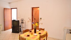 Un comedor con una mesa preparada para cuatro personas, un televisor y un florero con flores.
