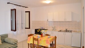 Una cocina compacta con armarios blancos, una mesa de comedor con sillas, un sofá y una ventana con cortinas.