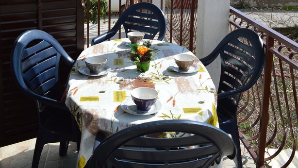 Un área de comedor al aire libre con una mesa preparada para cuatro personas, rodeada de sillas, bajo un porche cubierto.