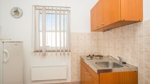 Une cuisine compacte dotée d’un évier encastré, de meubles en bois, d’un radiateur et d’une fenêtre avec des stores.