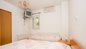Une chambre avec deux lits, un téléviseur fixé au mur et une fenêtre avec des volets.