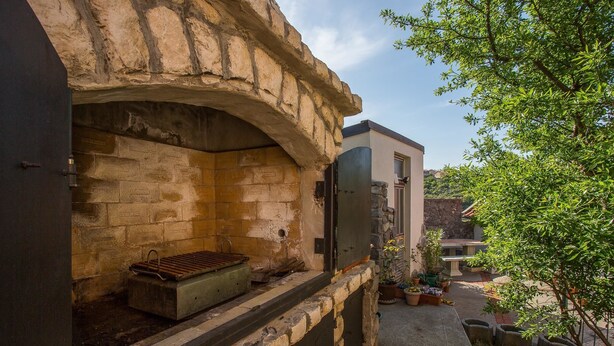 Un four en pierre avec un plateau en métal, un petit évier et une plante en pot sur un balcon.