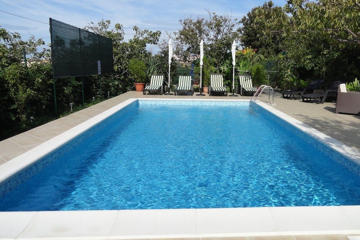 A rectangular swimming pool with clear blue water, surrounded by lounge chairs and umbrellas.