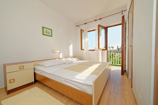 A bedroom with a wooden bed, a nightstand, a bedside table, and a view of the outdoors through an open door.