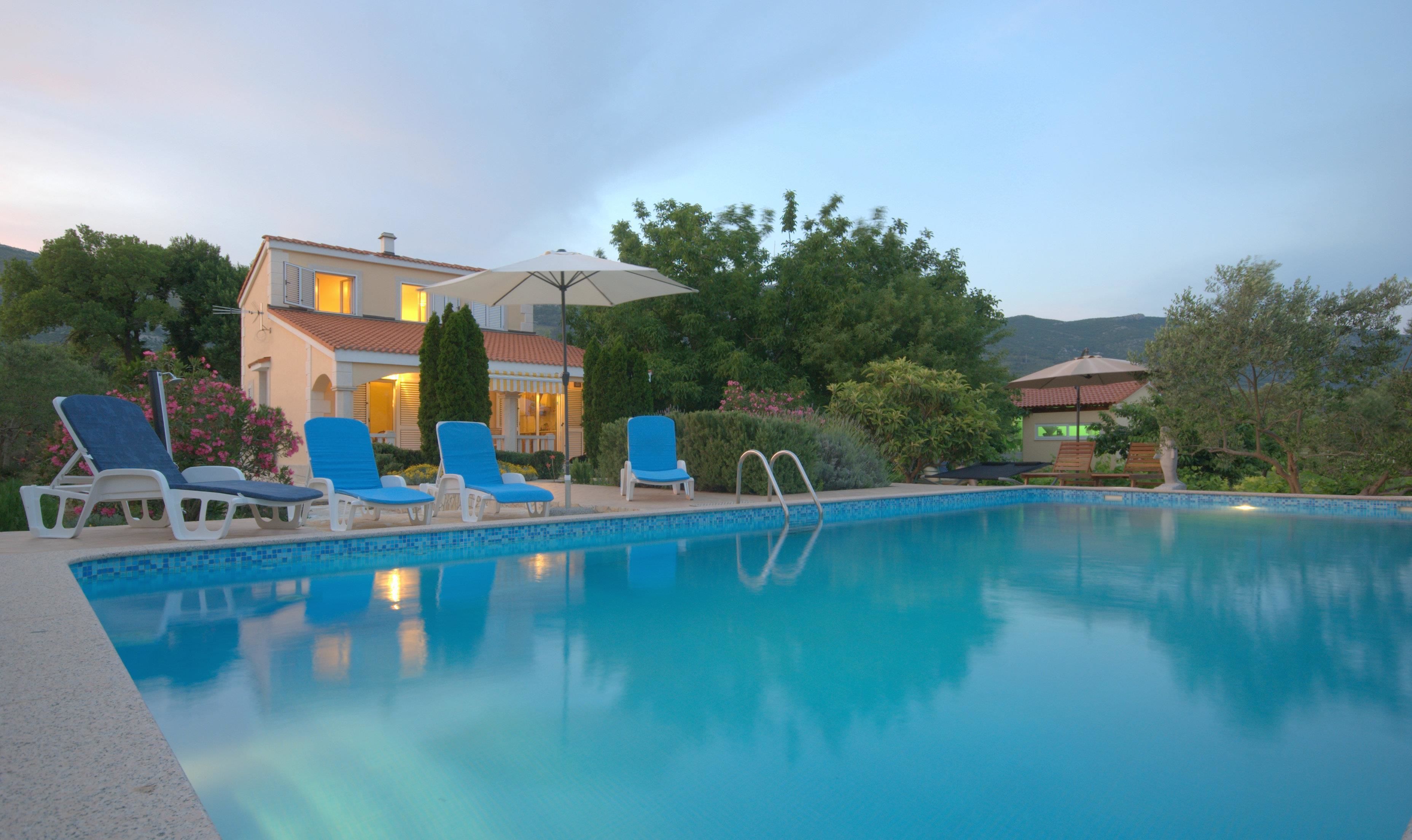 Una piscina con sillas de descanso y una casa al fondo.