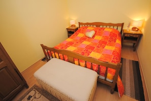 Un lit bien fait, recouvert d’une courtepointe, deux tables de chevet avec des lampes, un banc en bois et un tapis à motifs.