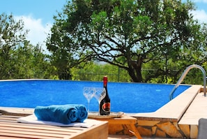 Une scène de bord de piscine avec une bouteille de champagne, un verre et une serviette posés sur une table en bois.