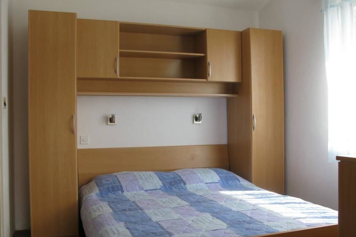 A bedroom with a bed, wooden wardrobe, and a shelf unit.