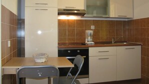 Una cocina compacta con armarios blancos, un horno, un lavamanos y una pequeña mesa de comedor con dos sillas.