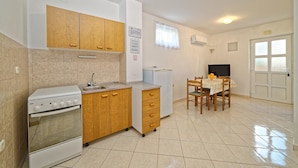 A compact kitchen with a stove, sink, wooden cabinets, a small refrigerator, and a dining table with chairs. - Apartments Biondić (Senj)