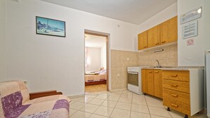 A compact kitchen with wooden cabinets and a built-in oven. A bed is visible in the adjacent room. - Apartments Biondić (Senj)