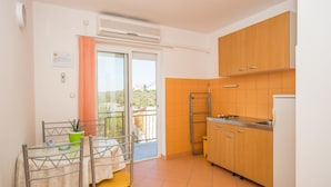 A compact kitchen with wooden cabinets, a built-in sink, and a small dining area with a table and chairs. - Apartments Biondić (Senj)