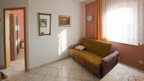 A living room with a sofa, a clock on the wall, and two framed pictures. - Apartments Pribil (Rab)
