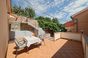A patio with a table and chairs, a stone wall, and a staircase with red railings. - Apartments Marica 3130 (Rab)
