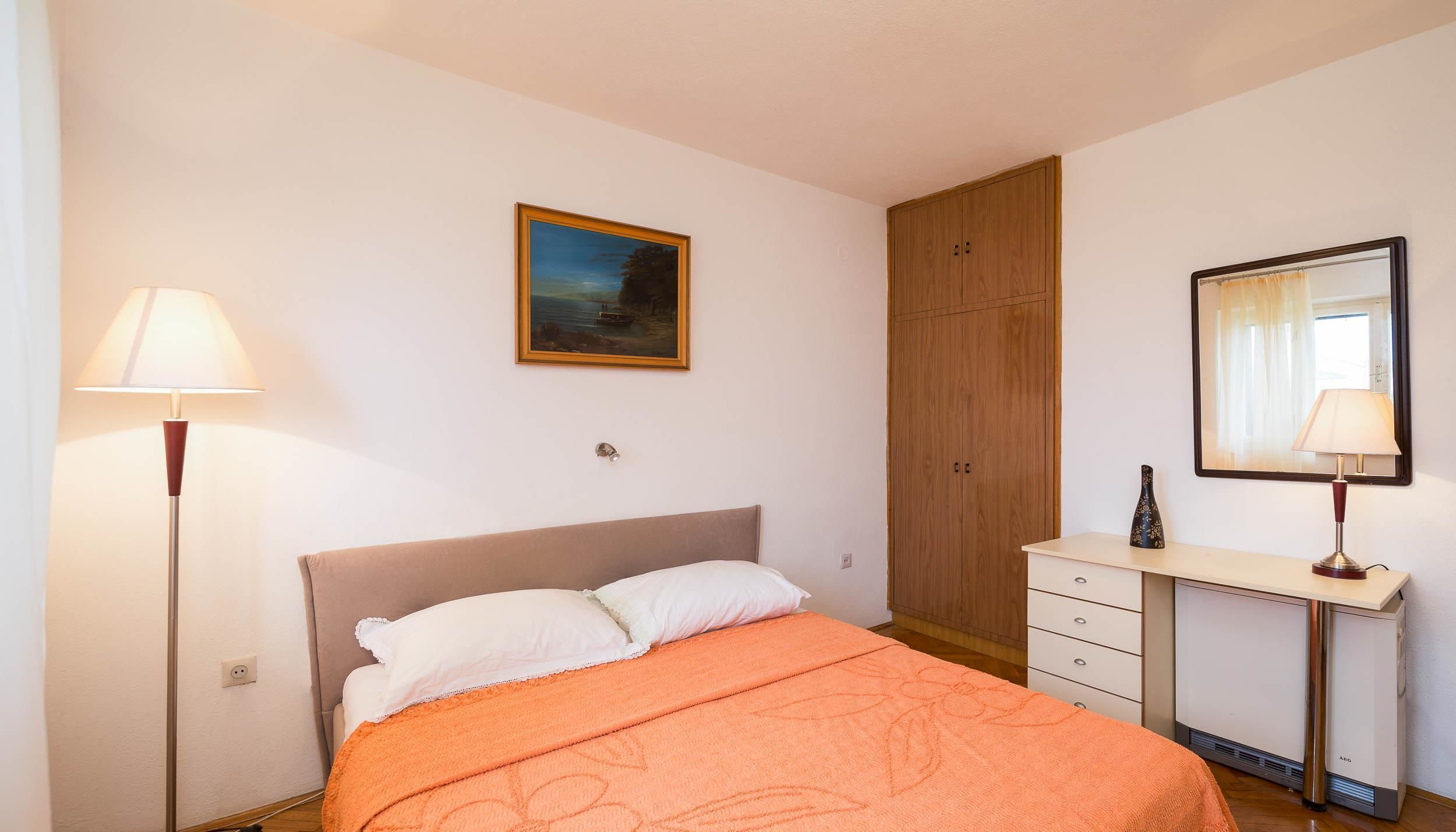 A bedroom with a bed, a nightstand, a dresser, a mirror, a painting, and a wardrobe.