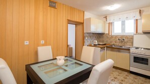 Une cuisine de taille réduite avec un lambris en bois, une table à manger avec des chaises, une cuisinière et une fenêtre avec des rideaux.