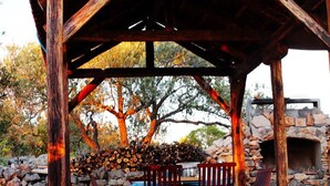 Un espacio de estar al aire libre rústico con muros de piedra y mobiliario de madera, todo bajo una pérgola de madera.