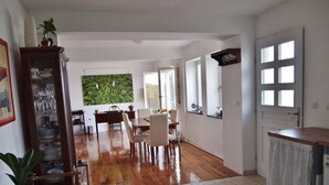 Amplia sala de estar con piso de madera, una mesa de comedor con sillas, una zona de cocina con ventanal y una puerta con ventana.