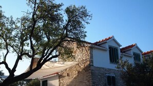 Una casa de piedra con tejado de tejas rojas, fachada blanca y un gran árbol en primer plano.
