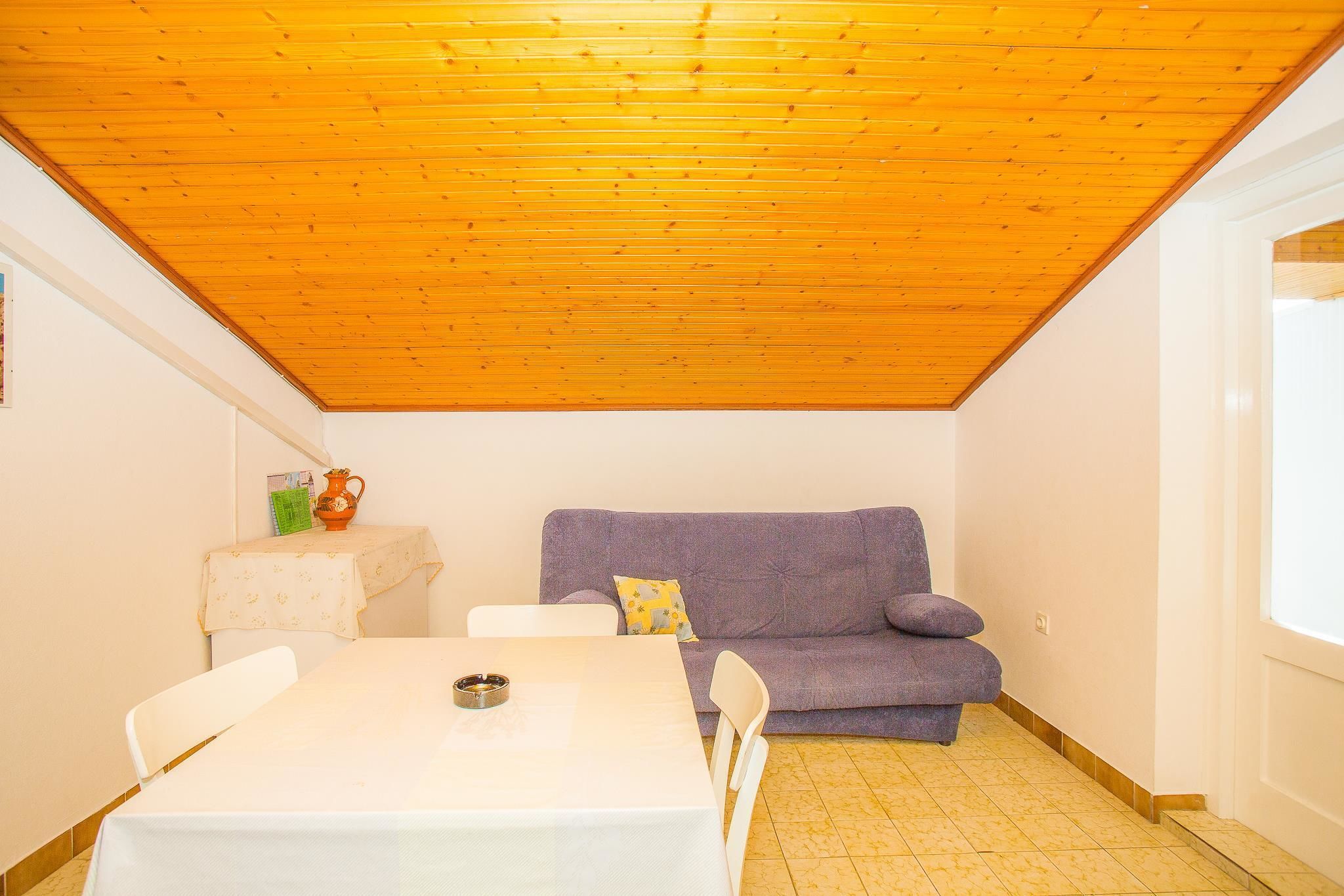 Une petite pièce avec un plafond en bois, un canapé violet, une table blanche et un sol carrelé.