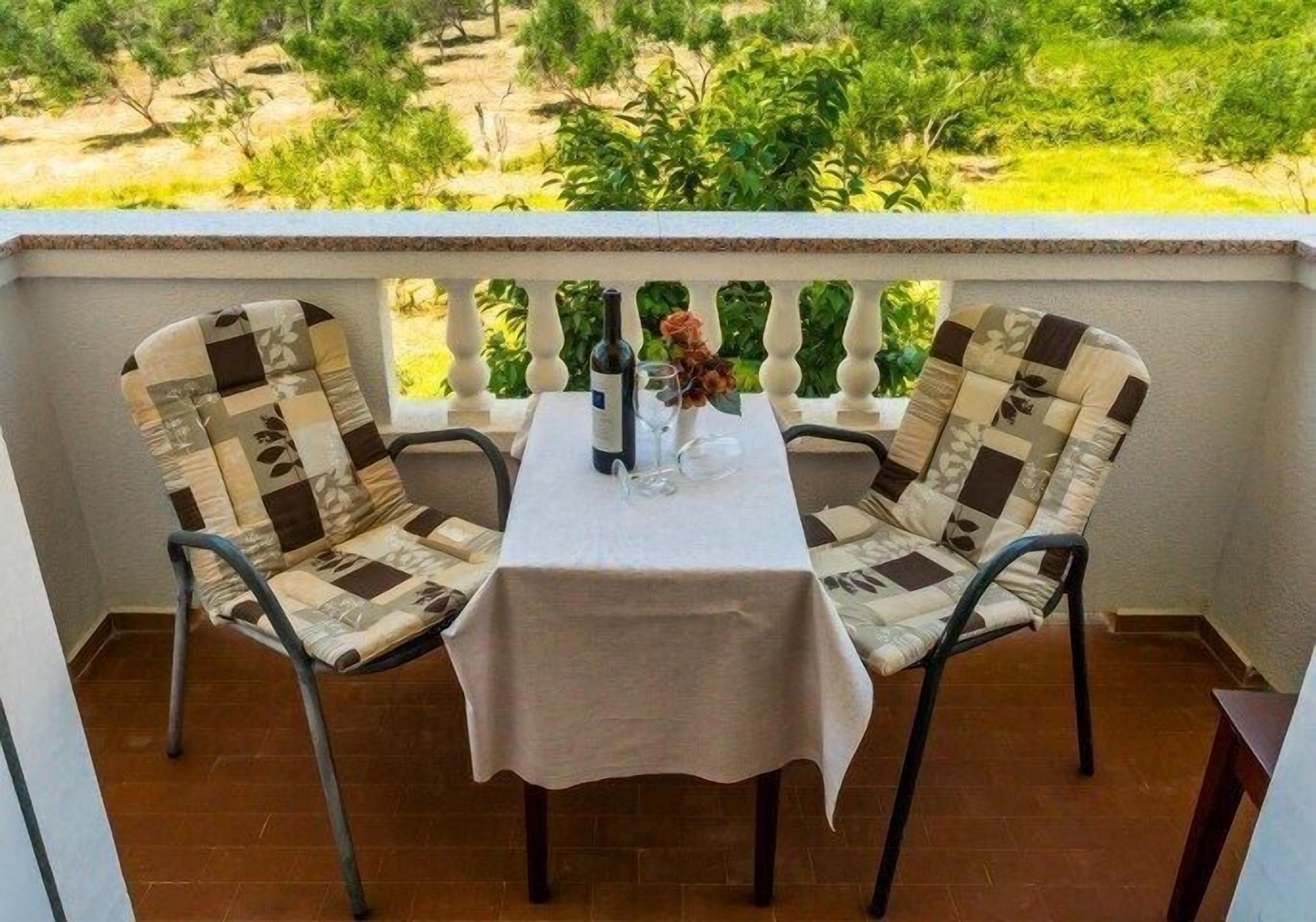 Een balkon met twee stoelen en een tafel, een fles wijn en een glas op de tafel.