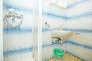 Un baño con ducha, lavabo y un cubo de basura verde.