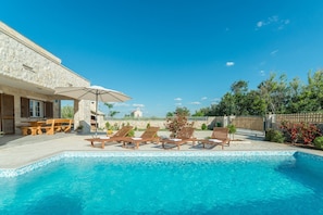 A pool area with lounge chairs and a table, surrounded by stone walls and greenery. - Villa St.vid 2 (Vir)