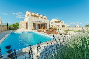A poolside area with a stone building, outdoor seating, and a clear blue sky. - Villa St.vid 2 (Vir)
