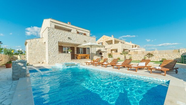 Un área junto a la piscina con sillones de descanso y un edificio de piedra.