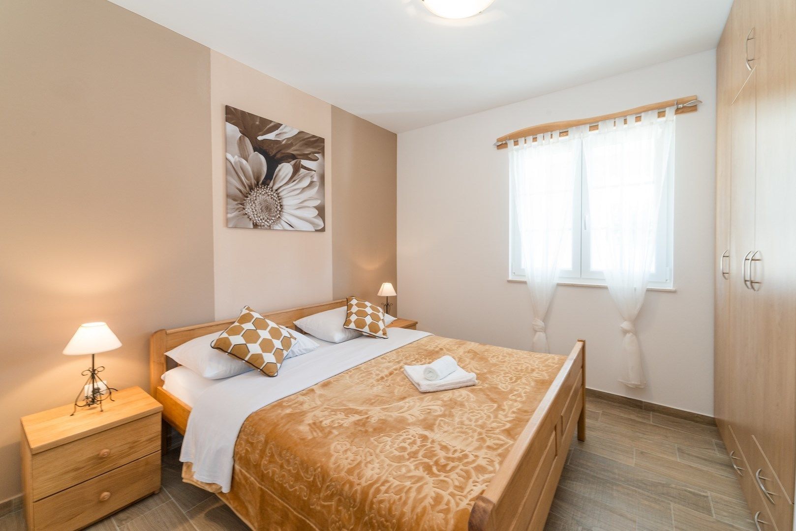 A bedroom with a bed, bedside lamps, a nightstand, a wooden wardrobe, and a window with curtains.