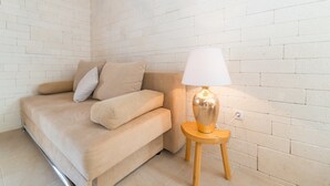 En beige sofa med puder, en lille træskammel og en bordlampe foran en hvid murstensvæg.