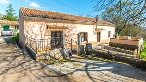 A small, single-story building with a tiled roof, a front entrance, and a small porch with a metal railing. - Holiday House Valter (Rasa)